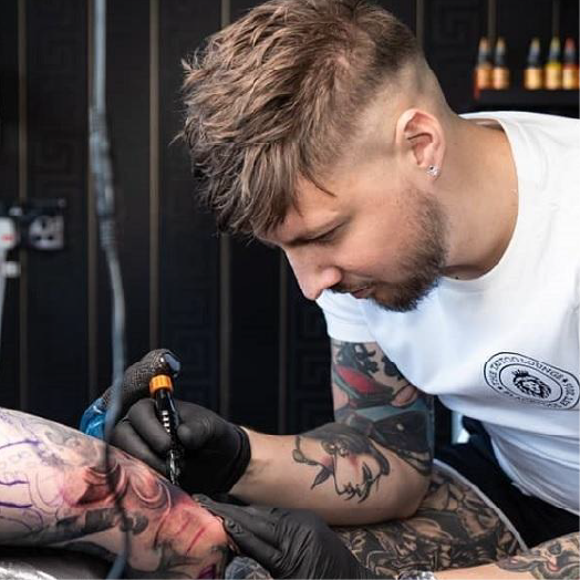 A man concentrating whilst doing a tattoo on a client in a high street tattoo parlour
